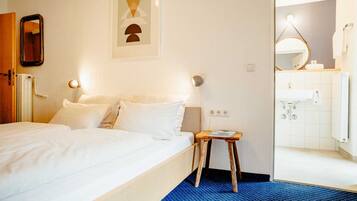 Een hotelkamer met een bed, nachtkastje, een spiegel aan de muur, en een badkamer zichtbaar door een geopende deur.