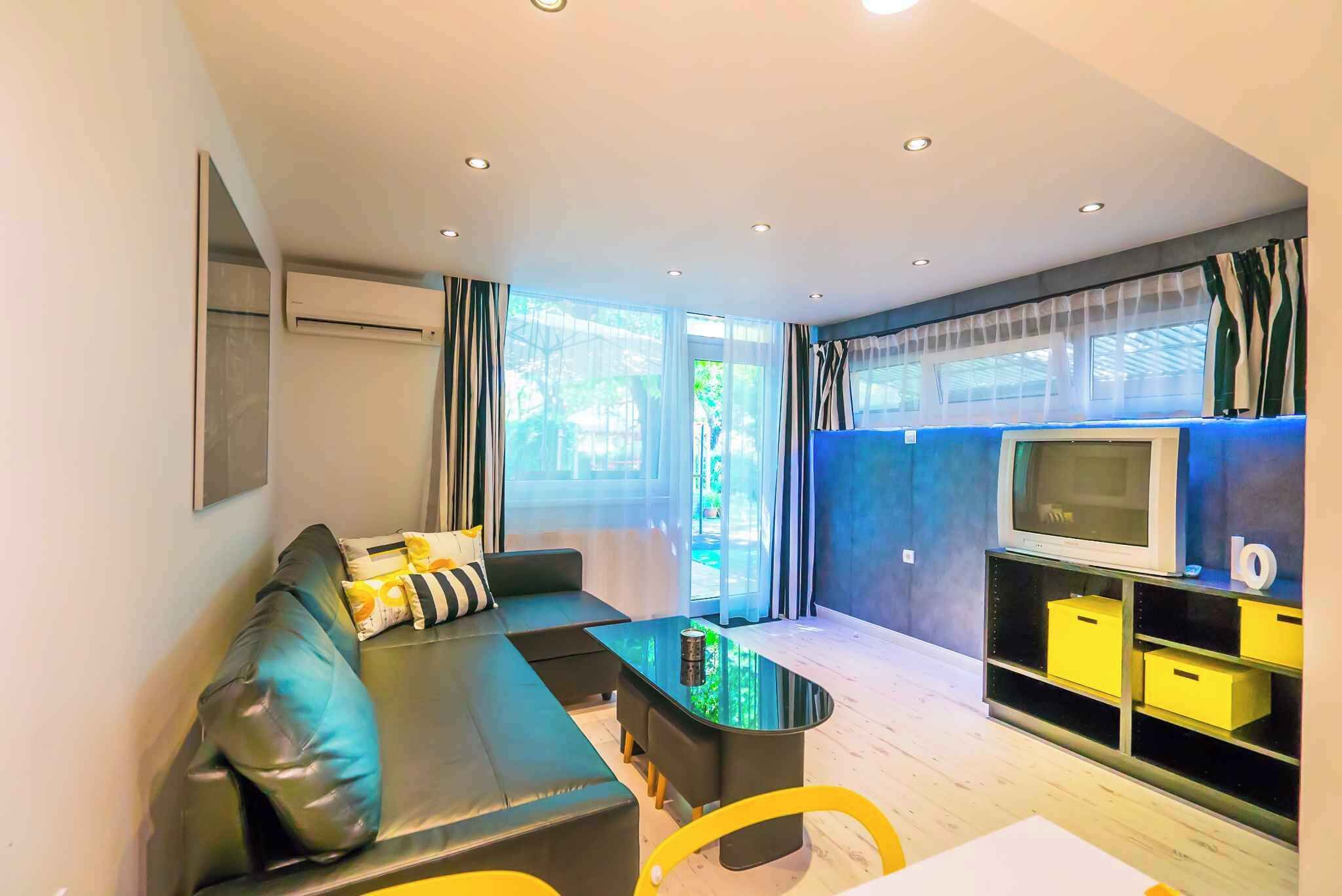 Una sala de estar moderna con un sofá negro, una mesa de centro de vidrio y un televisor sobre un mueble azul.