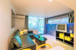 A modern living room with a black sofa, a glass coffee table, and a TV on a blue stand. - Holiday apartment only 250 m from the sandy beach on the Gold Coast (Siófok)
