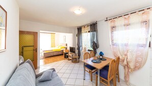 Een gezellige woonkamer met een bank, een eettafel met stoelen en een keuken op de achtergrond.