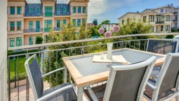 Ein Balkon mit Tisch und Stühlen, mit Blick auf eine Reihe von Gebäuden mit mehreren Etagen und Balkonen.