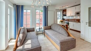 Ein modernes Wohnzimmer mit Ecksofa, Glastisch und moderner Pendelleuchte.