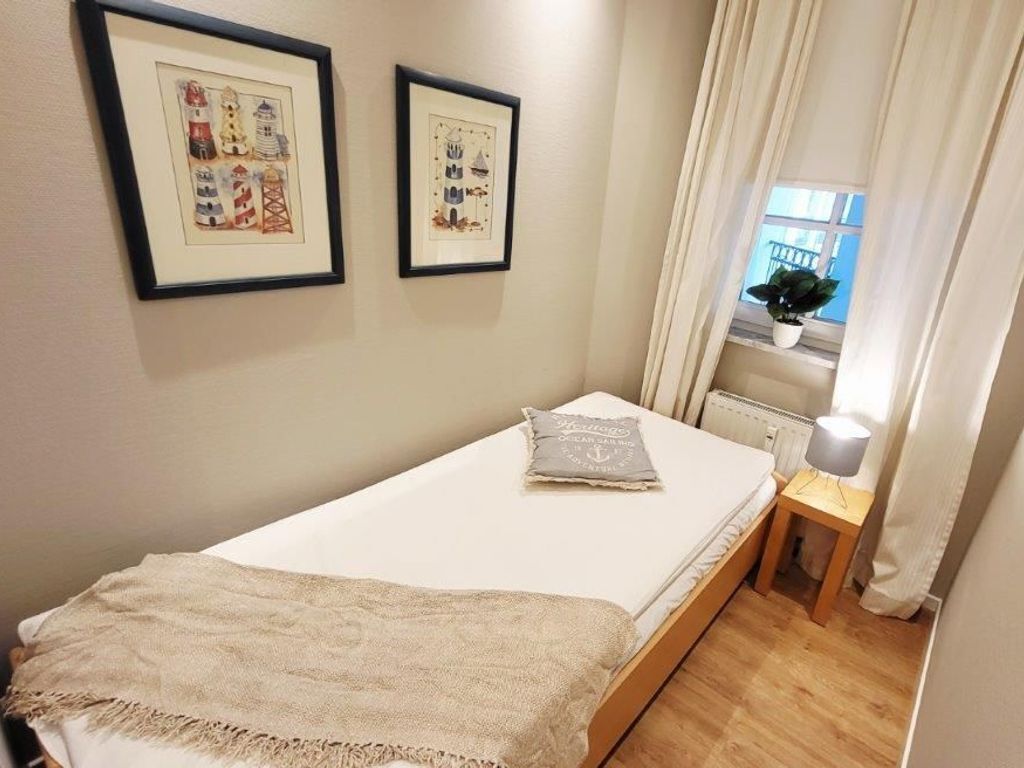 Un dormitorio pequeño y ordenado con una cama individual, una mesita de noche con lámpara y dos cuadros en la pared.
