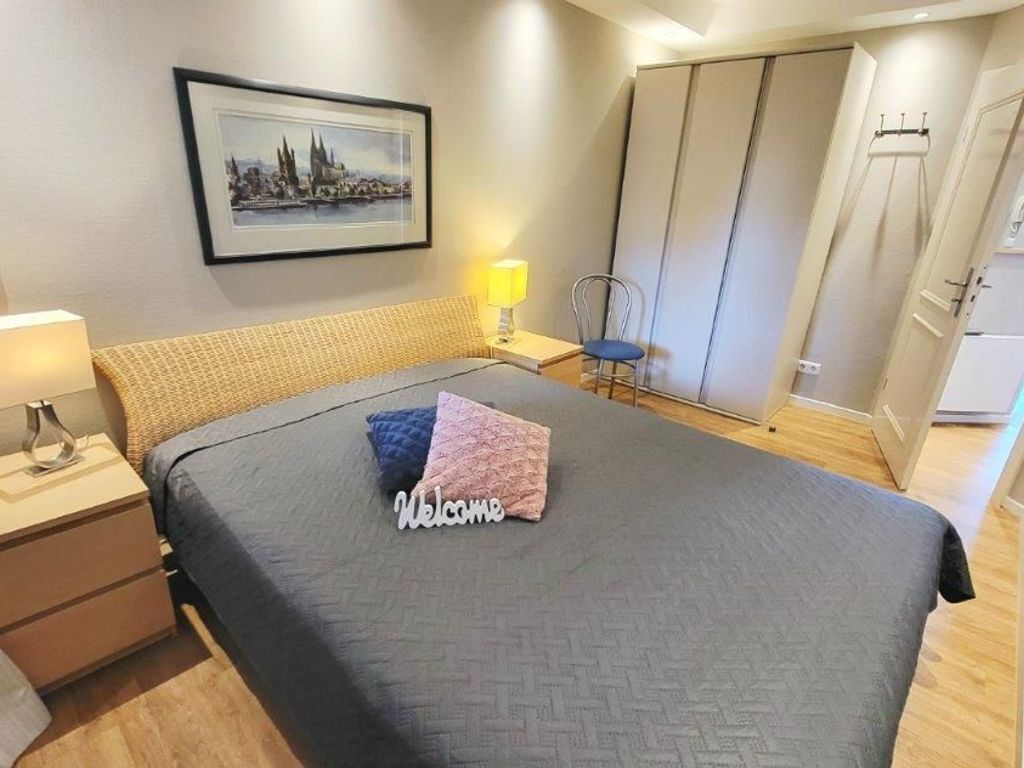 A neatly arranged bedroom with a bed, a bedside table with a lamp, a chair, a wardrobe, and a framed picture on the wall.