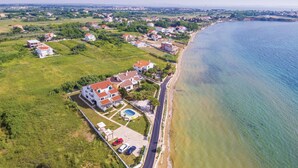 Vista aérea de una zona residencial costera con casas, una playa y un cielo despejado.