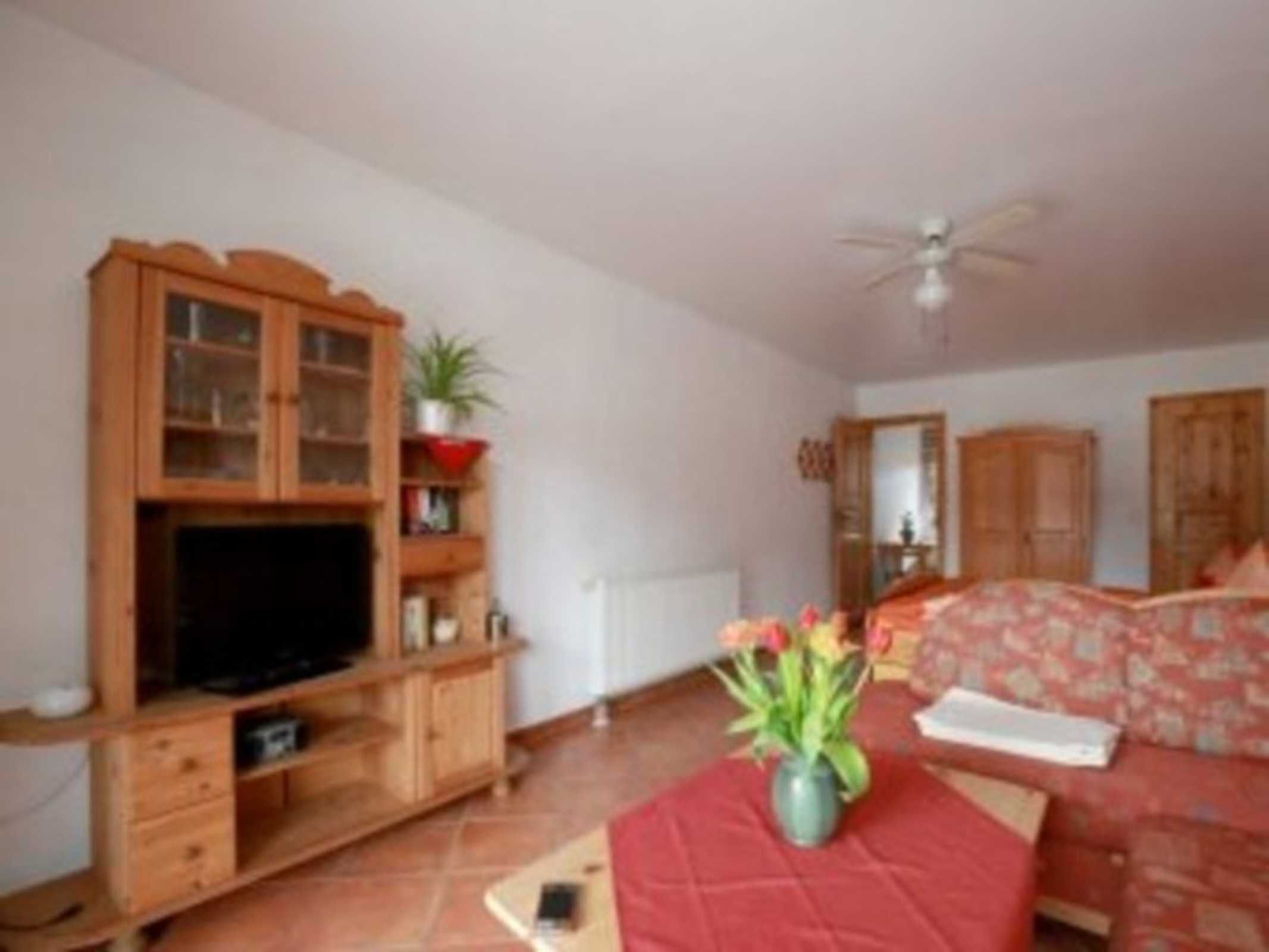A room with a wooden cabinet, a television, a red sofa, a ceiling fan, and a plant.