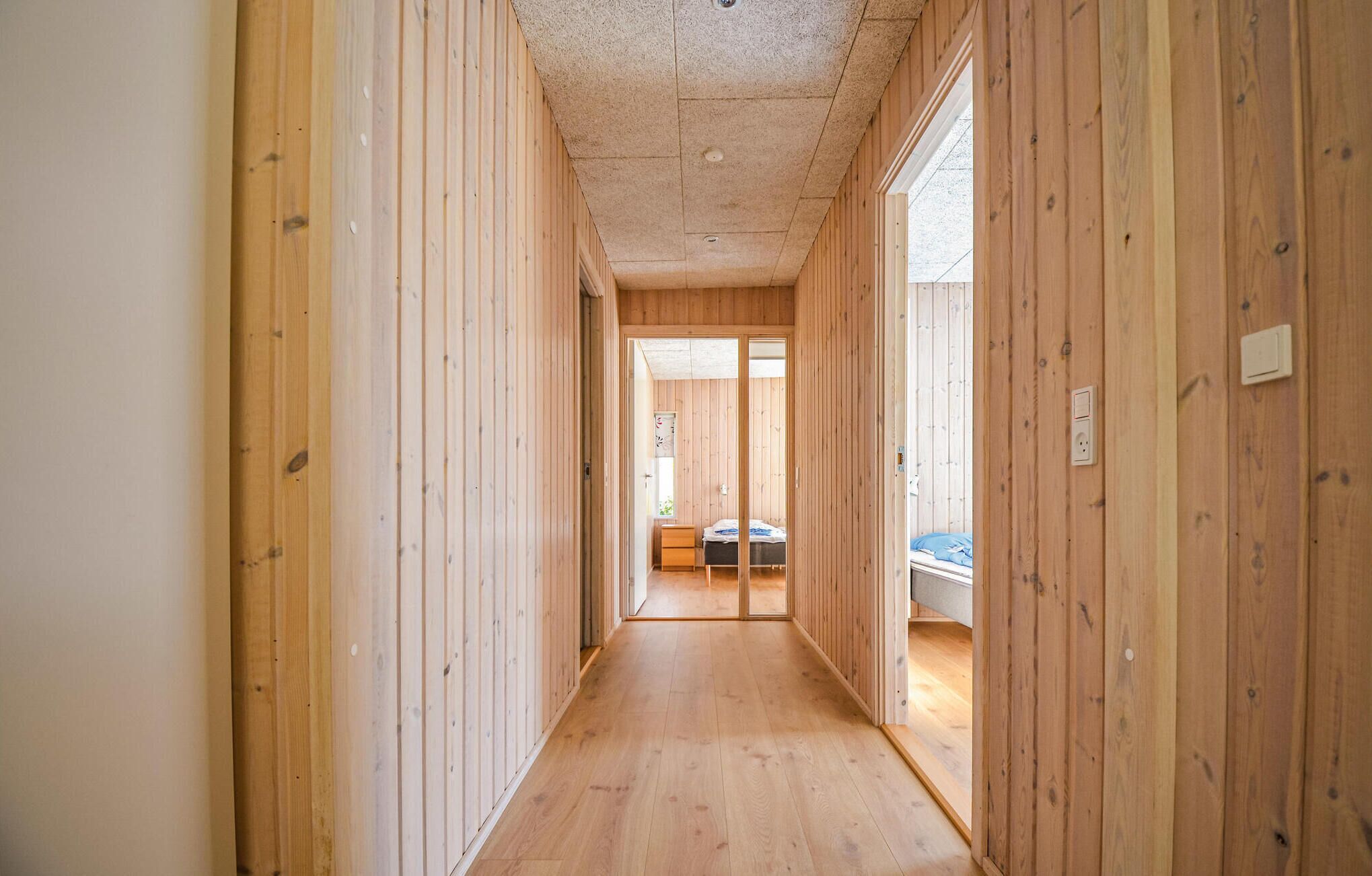 Un couloir étroit aux murs et au plancher en bois, qui mène à une pièce contenant un lit et une fenêtre.