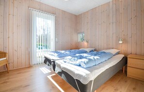 Une pièce aux murs en bois, un lit avec une literie bleue, une petite table de chevet, une chaise et une fenêtre avec des stores.