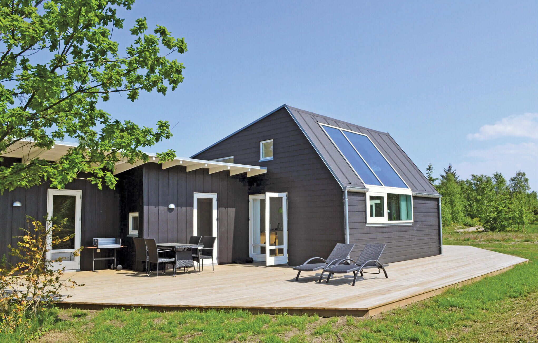 Ein modernes Haus mit dunkler Fassade, einer großen Terrasse, einem Essbereich mit Gartenmöbeln und einer Solaranlage auf dem Dach.