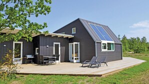 A modern house with a dark exterior, a large deck, a dining area with outdoor furniture, and a solar panel on the roof. - Beautiful home in Ebeltoft with kitchen (Ebeltoft)