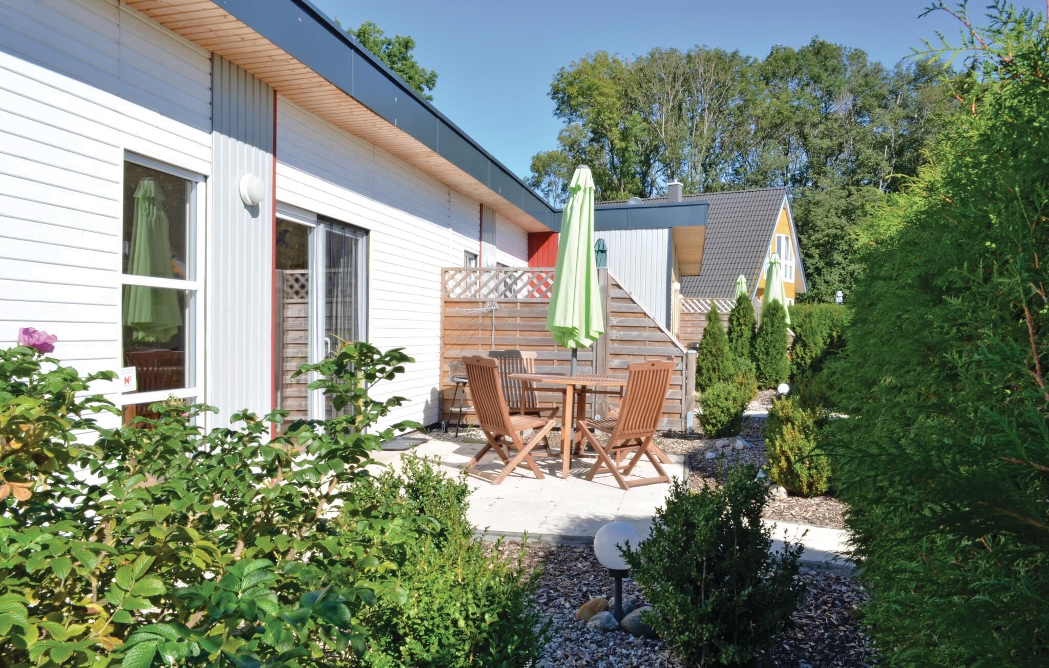 Ein Haus mit einer Terrassenfläche, ausgestattet mit Tisch und Stühlen, umgeben von Grünpflanzen und einem kleinen Garten.