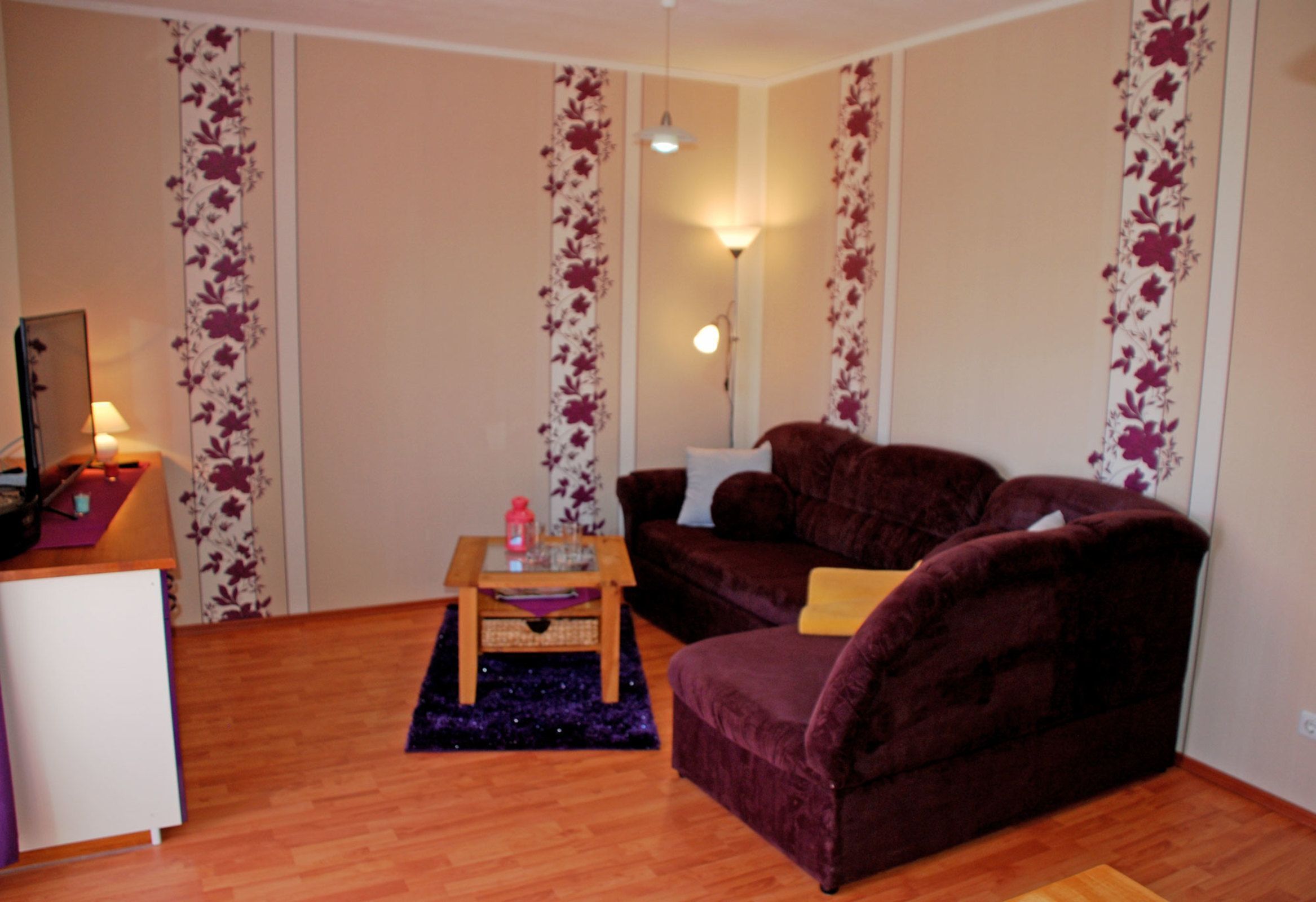 Ein Wohnzimmer mit einem violetten Sofa, einem kleinen Holztisch und einer Lampe.