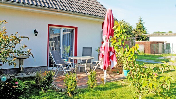 Una casa con techo de tejas, puerta de marco rojo y patio con mesa y sillas.