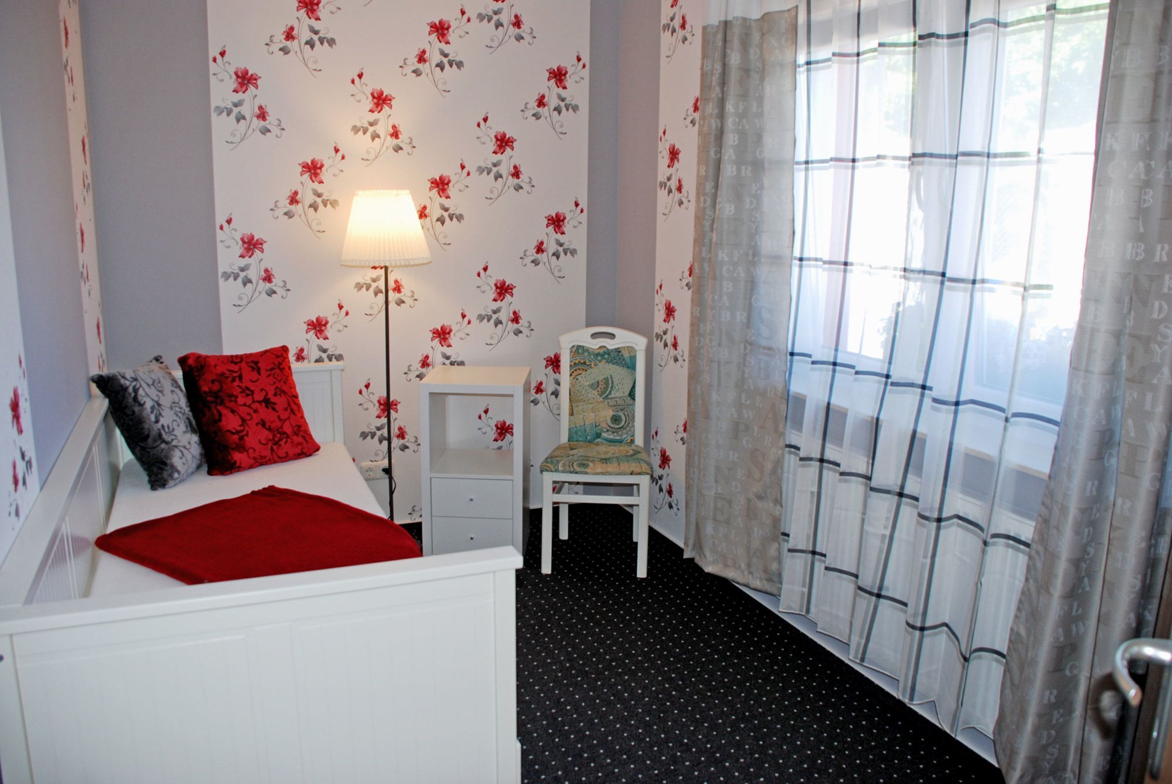 Une chambre à coucher avec un lit, une chaise, une lampe et une fenêtre avec des rideaux.