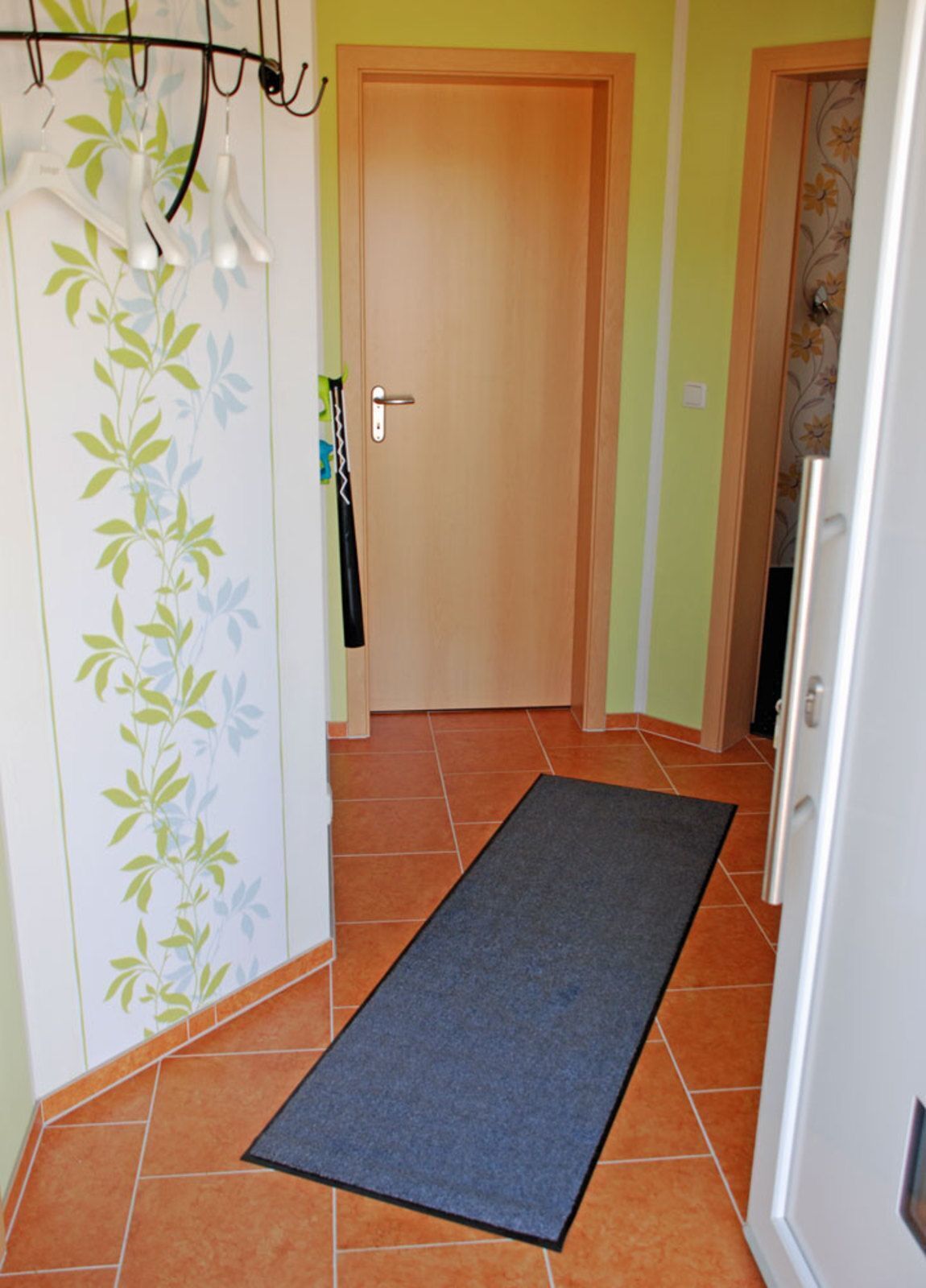 A hallway with a wooden door, a grey carpet, and a wall with a leafy pattern.