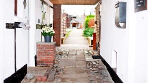 A narrow alleyway with a brick pathway, white walls, and a wooden ceiling. - Apartment East - Family Jansen - Home sweet home (Maasholm)