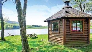 A small wooden cabin with a chimney, situated by a lake with a picnic table nearby. - Nice apartment in Sandnes with WiFi (Sandnes)