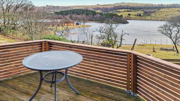 A wooden deck with a round table and chairs, overlooking a lake with a forested landscape in the background. - Nice apartment in Sandnes with WiFi (Sandnes)