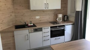 A compact kitchen with white cabinets, a coffee maker, and a dishwasher. - Apartment Type 1/2 + 1 ZuB - Meutzner Trassenheide, "Villa Seute Deern" (Trassenheide)