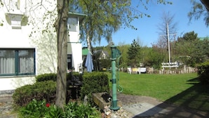 A house with a garden, a green outdoor water pump, and a white building in the background. - Apartment Type 1/2 + 1 ZuB - Meutzner Trassenheide, "Villa Seute Deern" (Trassenheide)