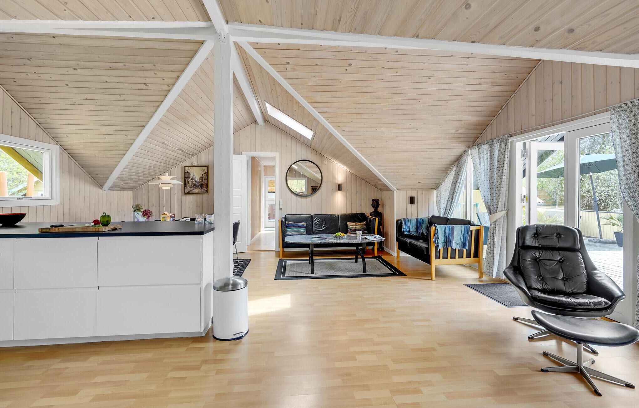 A spacious living area with a wooden ceiling, a dining table, a sofa, and a black leather chair.