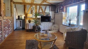 A cozy living area with exposed wooden beams, a TV, a dining table, and a wicker sofa. - Blue Water 2, Germany (Wustrow)