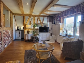 Una sala acogedora con vigas de madera a la vista, un televisor, una mesa de comedor y un sofá de mimbre.