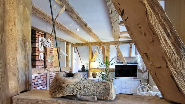A rustic interior with exposed wooden beams, a brick wall, a stone fireplace, a television, and a dining area. - Blue Water 2, Germany (Wustrow)