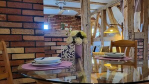 A dining area with a glass table, wooden chairs, a brick wall, and a hanging light fixture. - Blue Water 2, Germany (Wustrow)