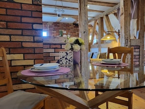 Un comedor con una mesa de vidrio, sillas de madera, una pared de ladrillo y una lámpara colgante.