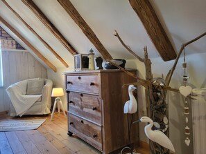 A loft bedroom with exposed wooden beams, a wooden dresser, a chair, and decorative items including a bird sculpture. - Blue Water 2, Germany (Wustrow)