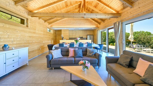 Een ruime woonkamer met hoog houten plafond, een eettafel voor zes personen en een bank met een bloevas.