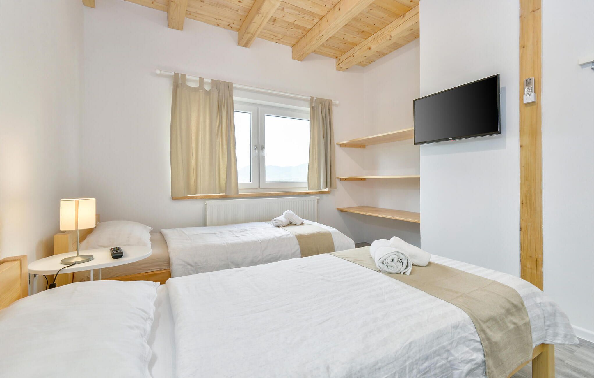 A hotel room with two beds, a TV, a desk with a lamp, and a window with curtains.