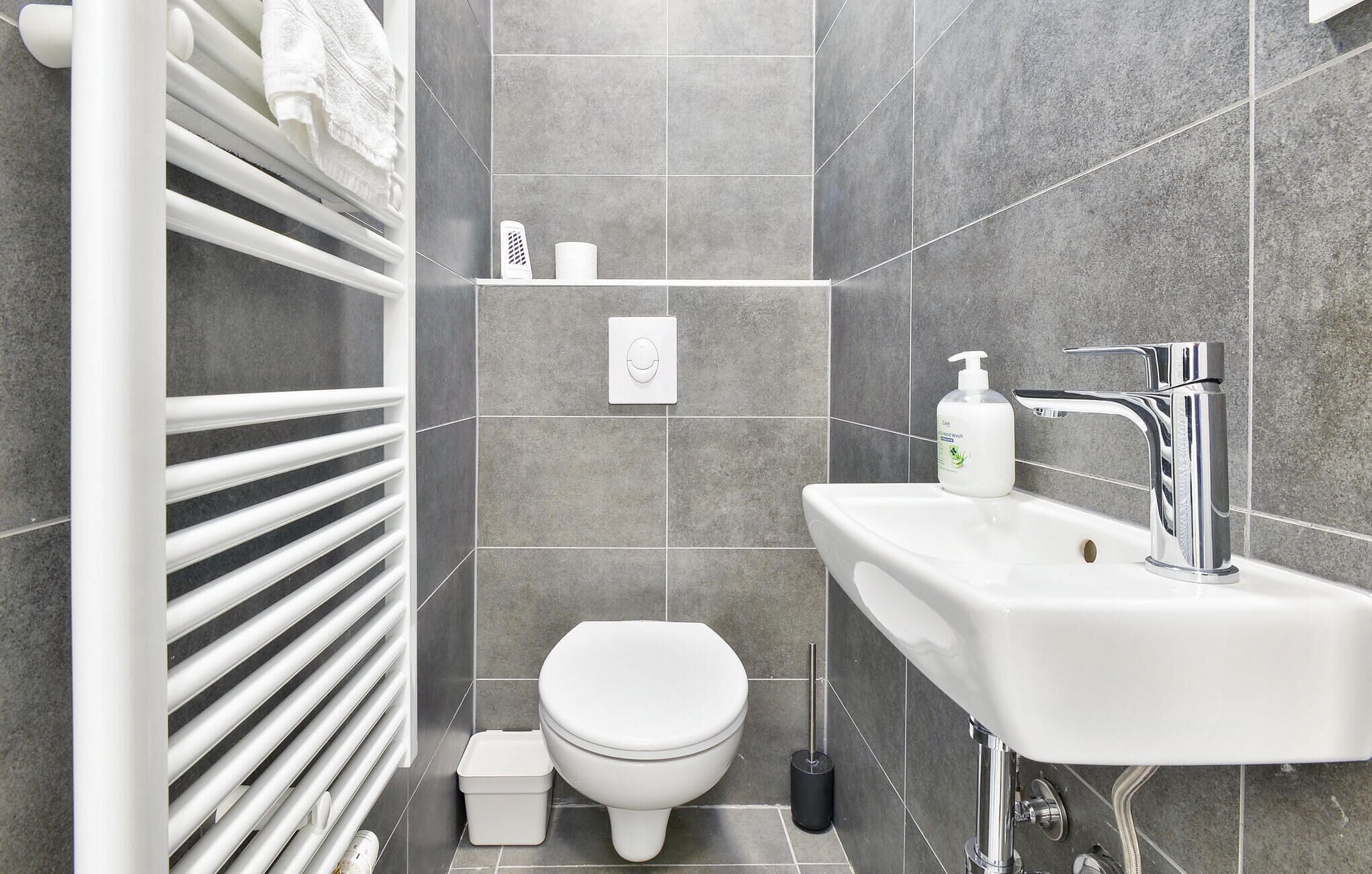 Une salle de bain moderne avec des toilettes blanches, un lavabo blanc doté d’un robinet chromé et un porte-serviettes avec des serviettes blanches.