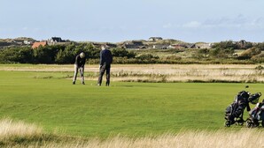 A golf course with a clear sky, a few houses in the background, and a golf bag in the foreground. - Nice home in Ringkøbing with sauna (Ringkøbing)