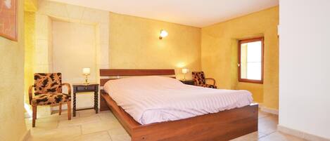 A bedroom with a wooden bed, two nightstands, a chair, a window, and a wall-mounted light.