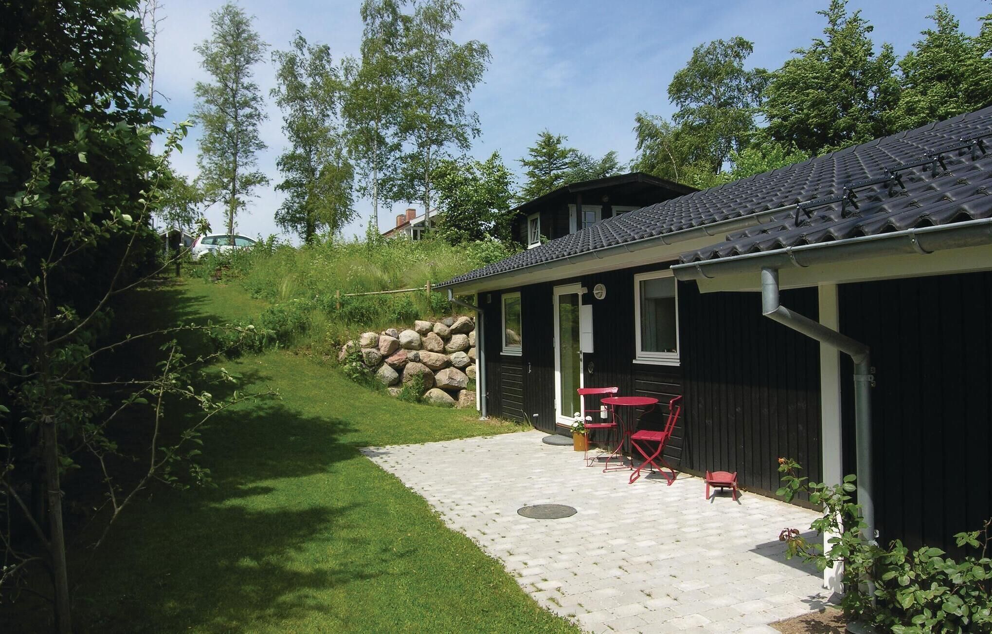 Ein Haus mit einer Terrasse, ausgestattet mit einem Kiesweg, einem kleinen Tisch und roten Stühlen.
