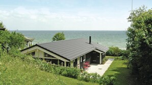 Une maison située sur la côte, avec un toit sombre, une cheminée et une petite terrasse dotée de chaises rouges.