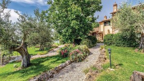 A rustic villa with a gravel pathway leading to the entrance, surrounded by lush greenery and flowering plants. - Nice home in Castiglione d.Lago PG (Castiglione d.Lago PG)