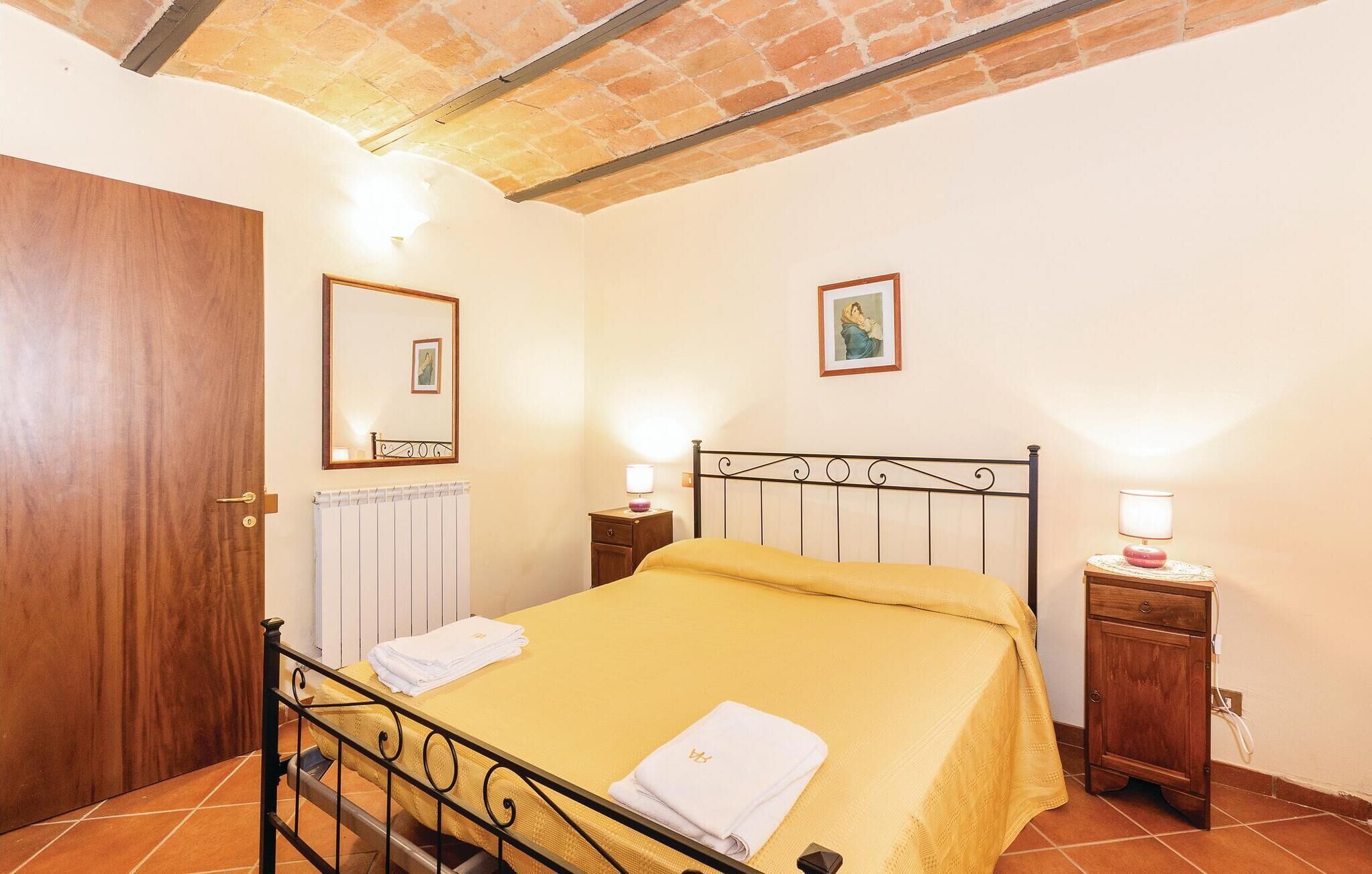 Un dormitorio con una cama, una puerta de madera, un radiador, una mesita de noche con una lámpara y un armario pequeño.