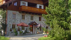 A stone building with a wooden balcony, outdoor seating, and a red car parked in front. - Dachsteinblick - Organic Farm Mondsee Family Schafleitner-Kroiß (3 Flowers) (Guggenberg)