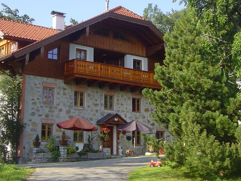 A stone building with a wooden balcony, outdoor seating, and a red car parked in front.