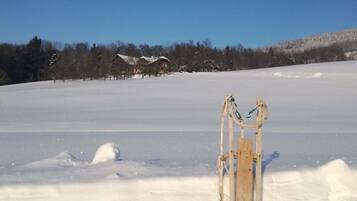 Schneebedeckte Landschaft mit einem Schlitten im Vordergrund und einem Haus im Hintergrund.
