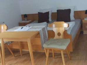 A hotel room with a wooden bed, a wooden nightstand with a lamp, a wooden table, and a chair.