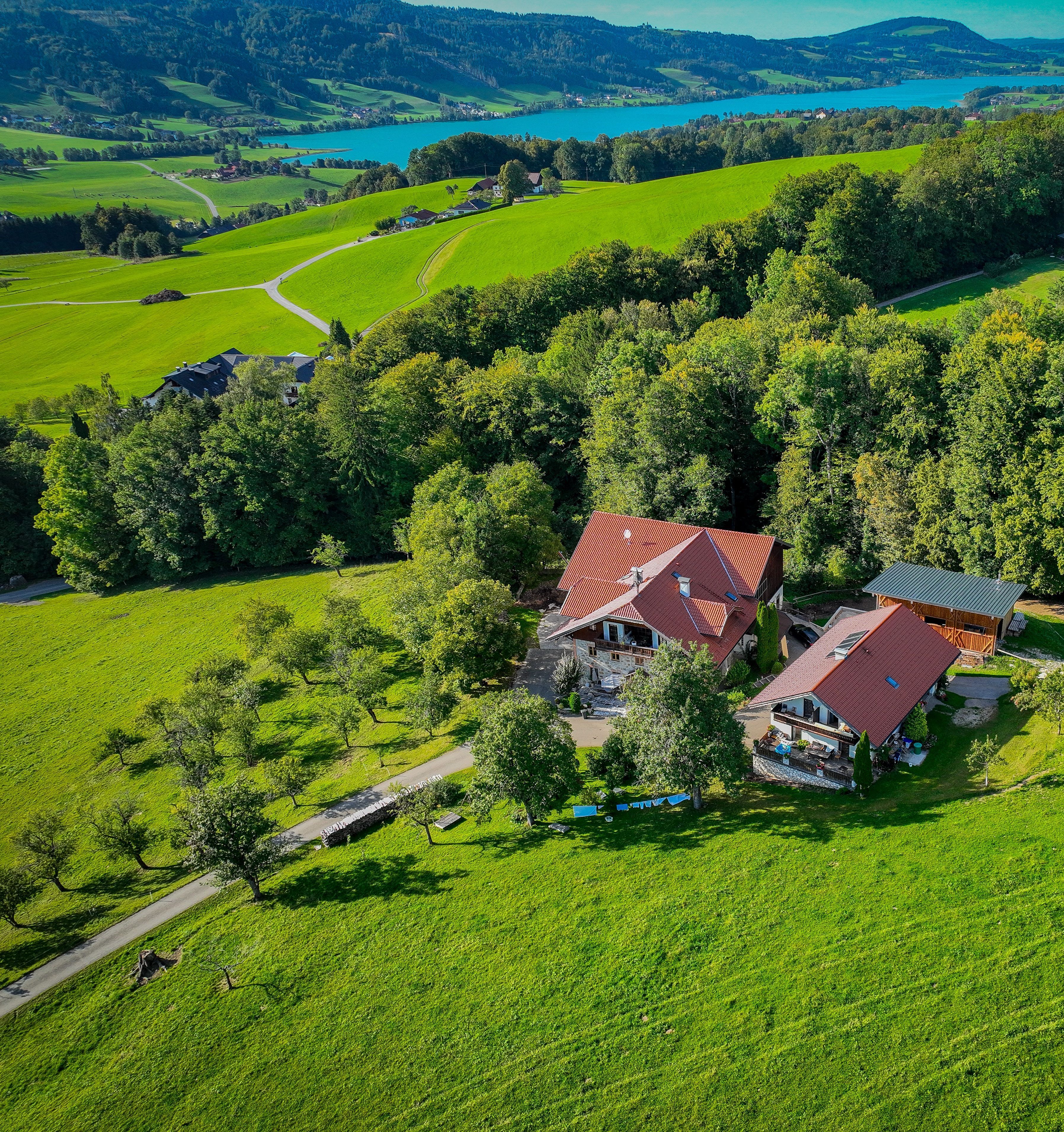 Eine Luftaufnahme einer ländlichen Anlage mit zwei Hauptgebäuden, einem weitläufigen Feld und einem See im Hintergrund.