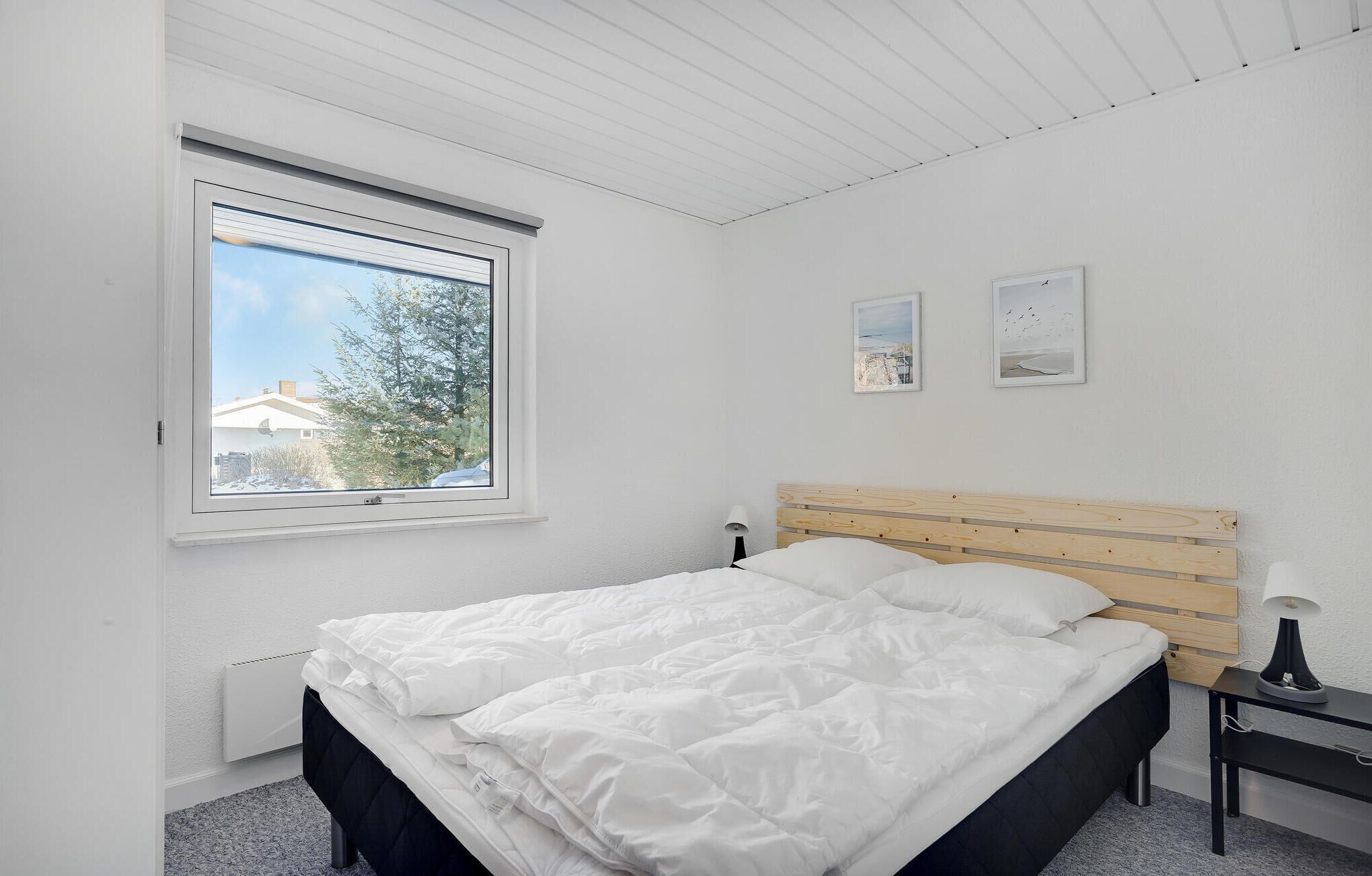 A bedroom with a bed, a nightstand, a lamp, and a window with a view of trees and buildings.