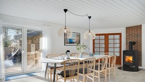 Un espace repas comprenant une table, des chaises, des luminaires suspendus et un poêle à bois.
