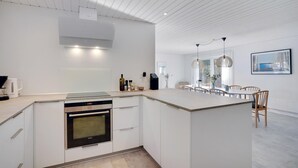 Une cuisine moderne avec des meubles blancs, un four encastré et un coin repas comprenant des chaises et une table en bois.