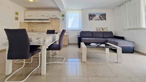 A modern living room with a dining area, a sofa, and a kitchen in the background. - Holiday apartment newly furnished for 2-4 pers. with air conditioning, WLAN and car park (Baška)
