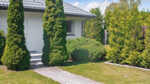 Uma casa com um caminho de entrada pavimentado que leva a uma porta da frente, cercada por vegetação bem cuidada e uma cerca de metal.